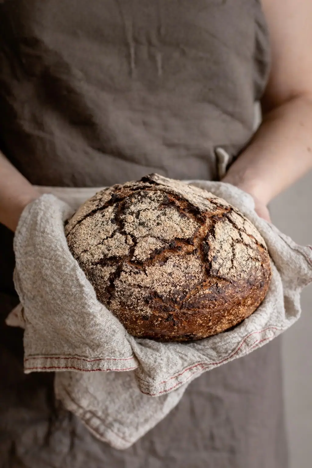 A baker holding a fresh rye loaf in a linen cloth